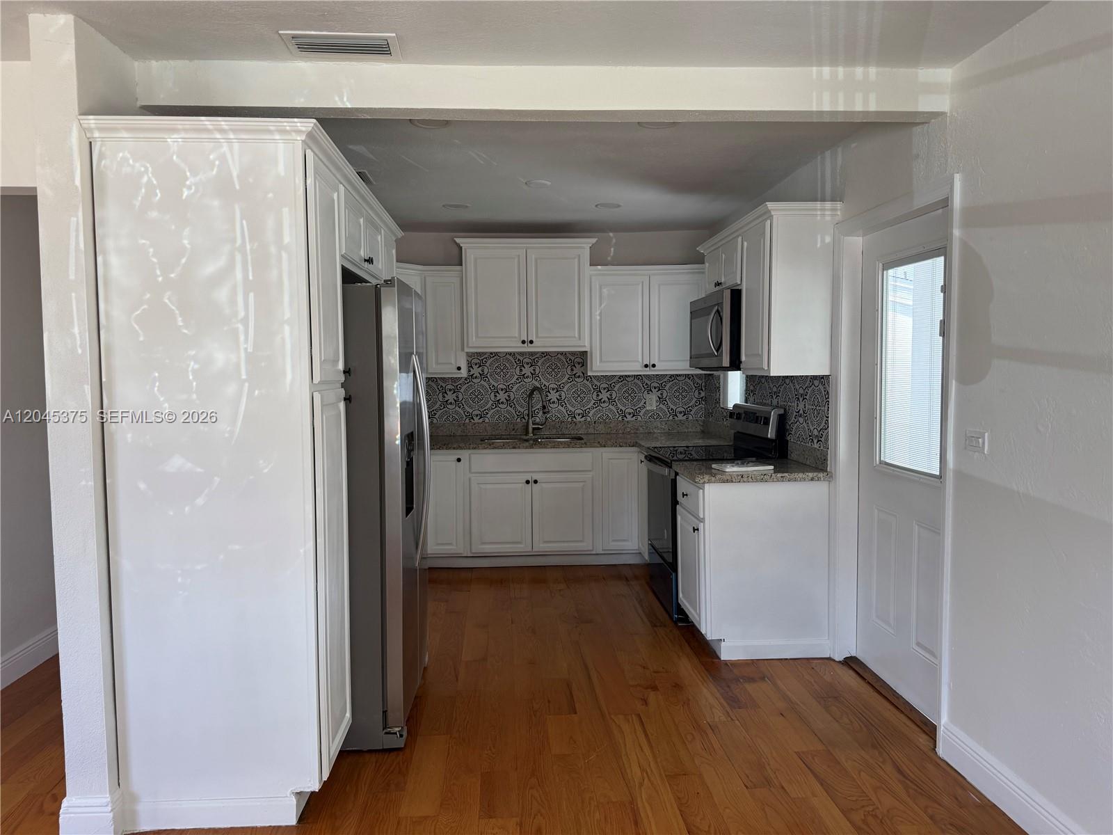 A kitchen features white cabinets, stainless steel appliances, patterned tile backsplash, and hardwood flooring — 3500 SW 87th Pl # 3500, Miami FL 33165, MIAMI, FL