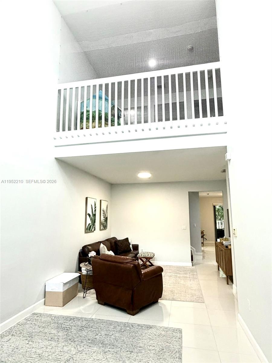A living room features white walls, tile flooring, a leather sofa, and a mezzanine balcony — 10780 NW 74th Ln, Doral FL 33178, DORAL, FL