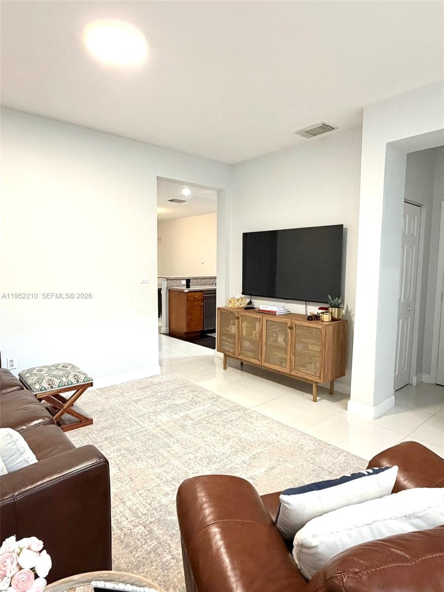 A living room features a brown leather sofa, a rattan media console, and tile flooring — 10780 NW 74th Ln, Doral FL 33178, DORAL, FL