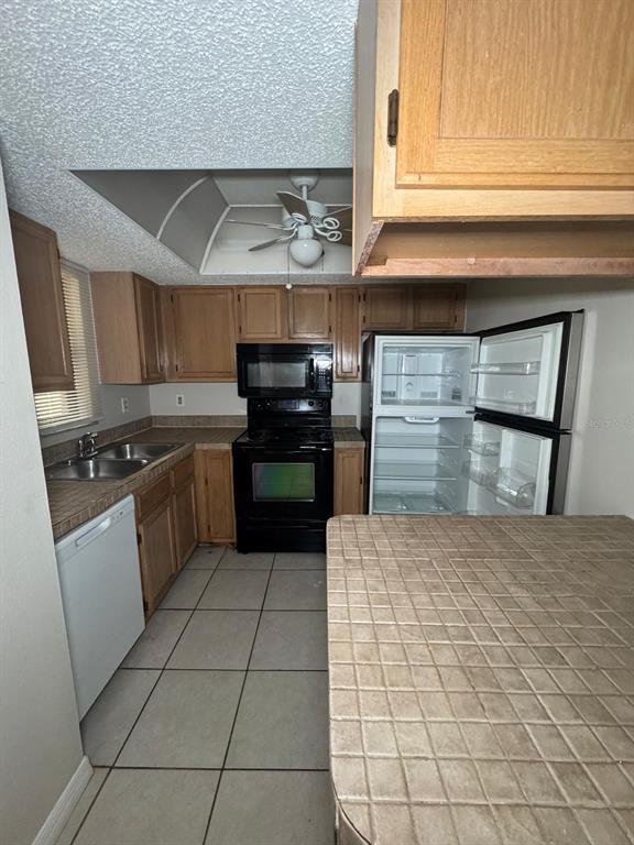 A kitchen features wood cabinets, tile countertops, a black appliance suite, and a tiled floor — 2416 SE GARDEN TERRACE UNIT 203, PORT ST LUCIE, FL