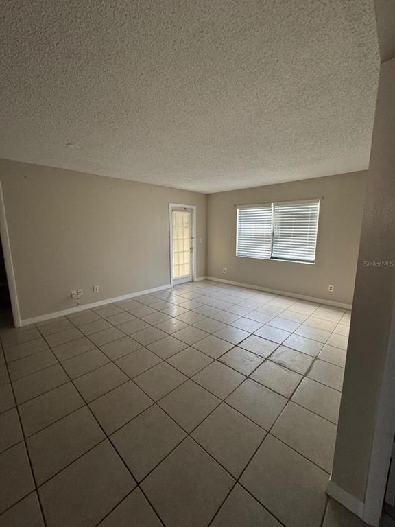 An empty room features beige walls, light-colored tile flooring, a glass-paneled door, and window blinds — 2416 SE GARDEN TERRACE UNIT 203, PORT ST LUCIE, FL