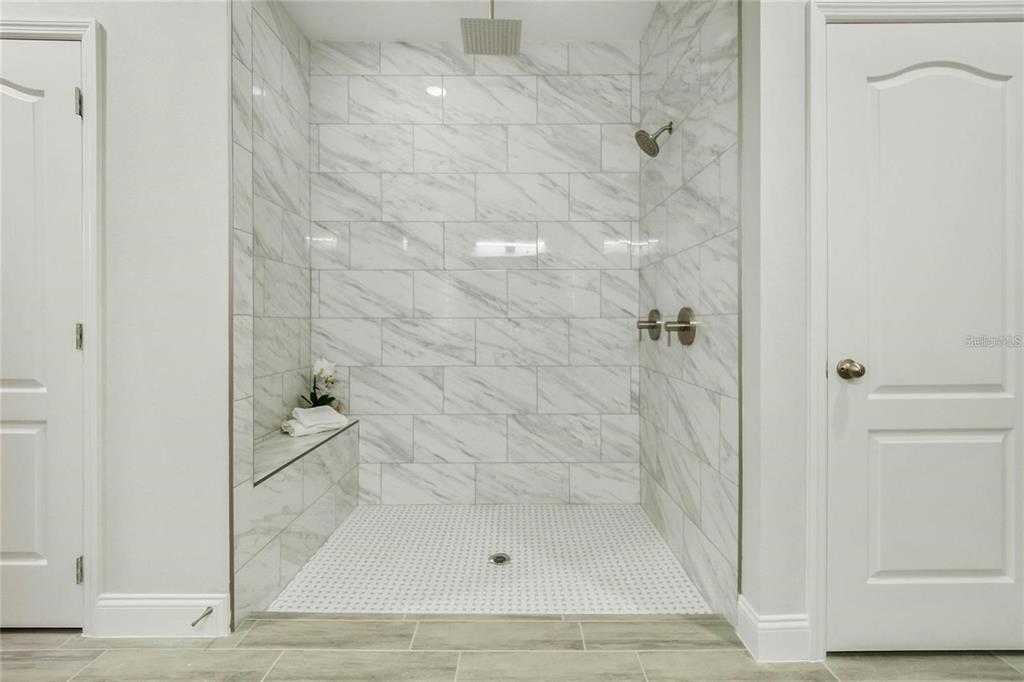A walk-in shower features white marble-look wall tiles, a built-in bench, and a mosaic floor — 2239 PECOS COURT, KISSIMMEE, FL