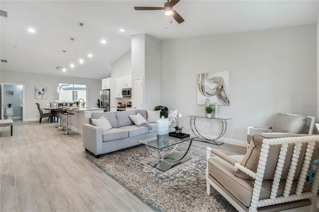 An open-concept living room features a grey sofa, a glass coffee table, and tile flooring — 2239 PECOS COURT, KISSIMMEE, FL