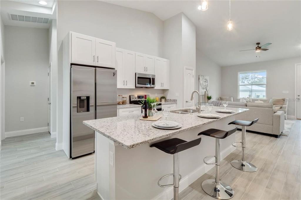 A kitchen with white cabinets, stainless steel appliances, and a granite-topped island with bar stools — 2239 PECOS COURT, KISSIMMEE, FL