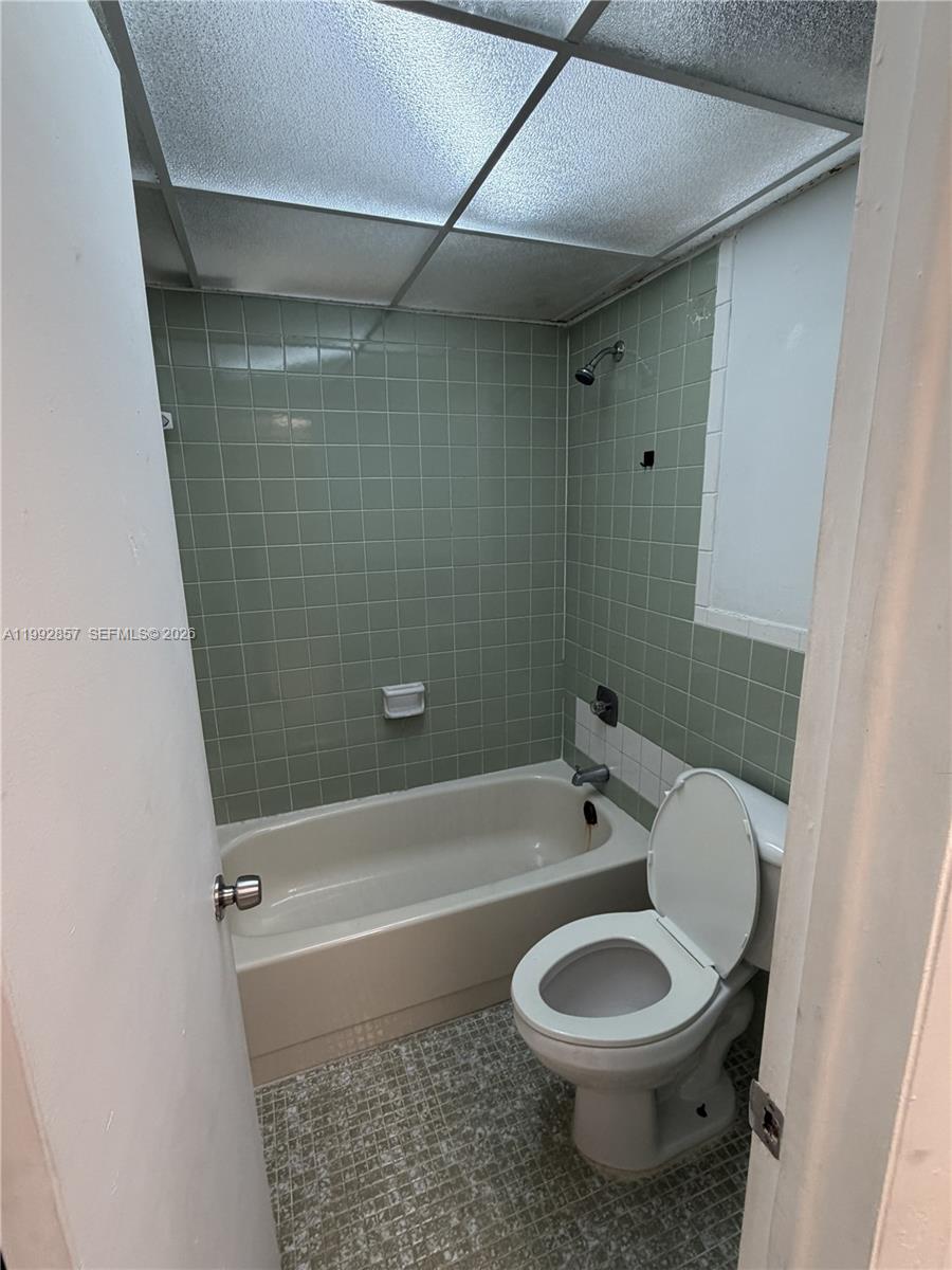 A bathroom features green tiled walls, a beige bathtub, and a white toilet — 7010 NW 186th St # 121A, Hialeah FL 33015, HIALEAH, FL