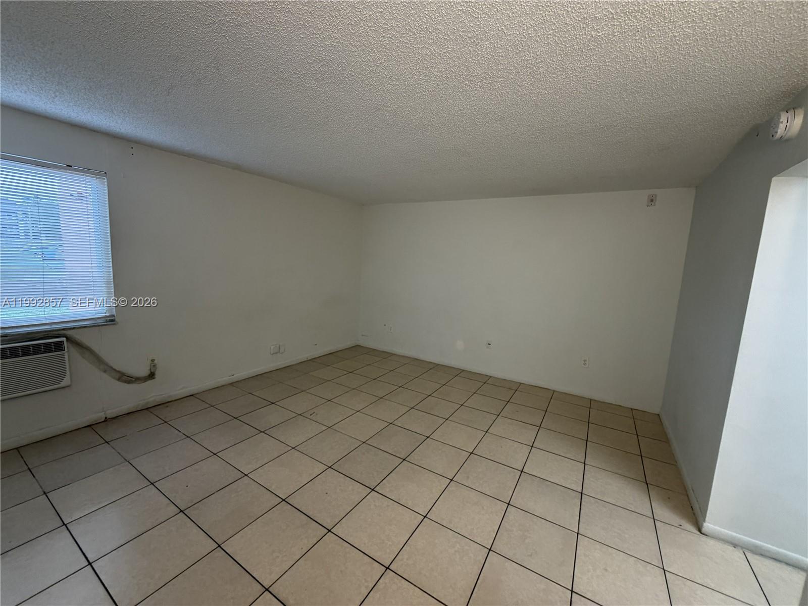 An empty room features white walls, beige tile flooring, and a window with blinds — 7010 NW 186th St # 121A, Hialeah FL 33015, HIALEAH, FL