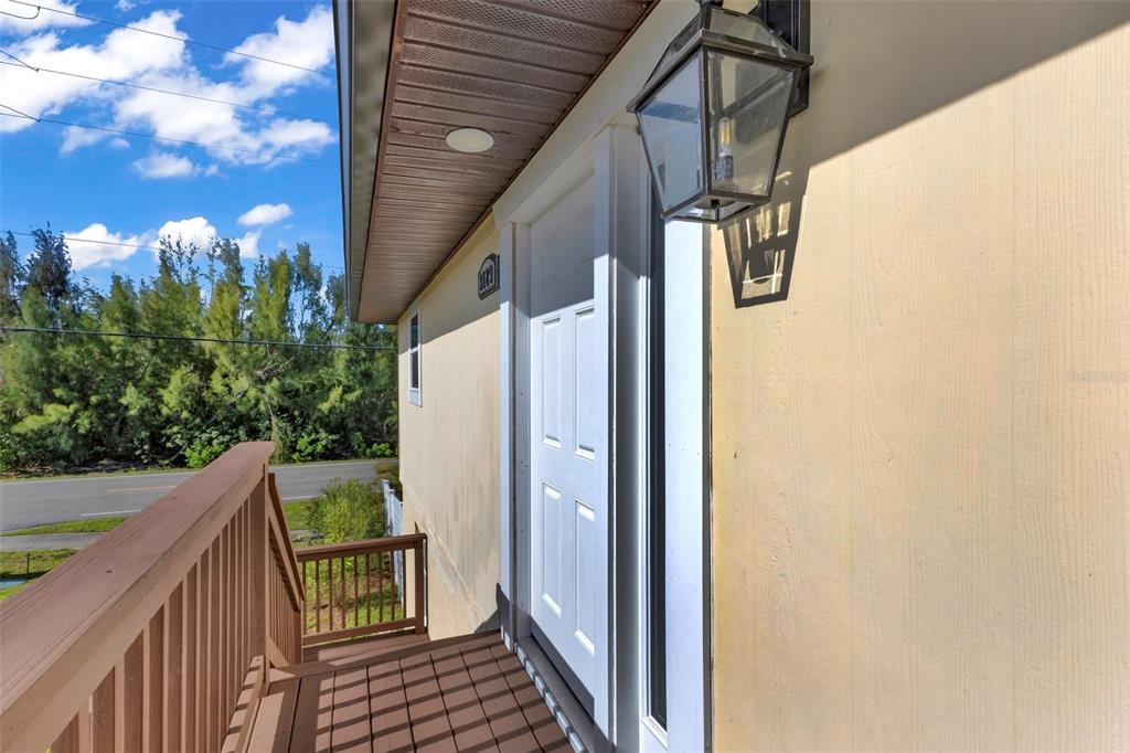 An exterior view of a wooden deck leading to a white door with a lantern — 3129 BANYAN WAY, PUNTA GORDA, FL