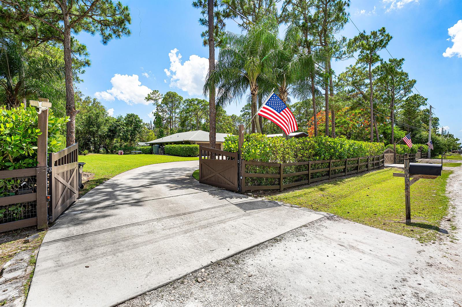 A concrete driveway leads through an open wooden gate toward a house behind a hedge — 13530 N 59th Ct Court N, FL 33411, FL