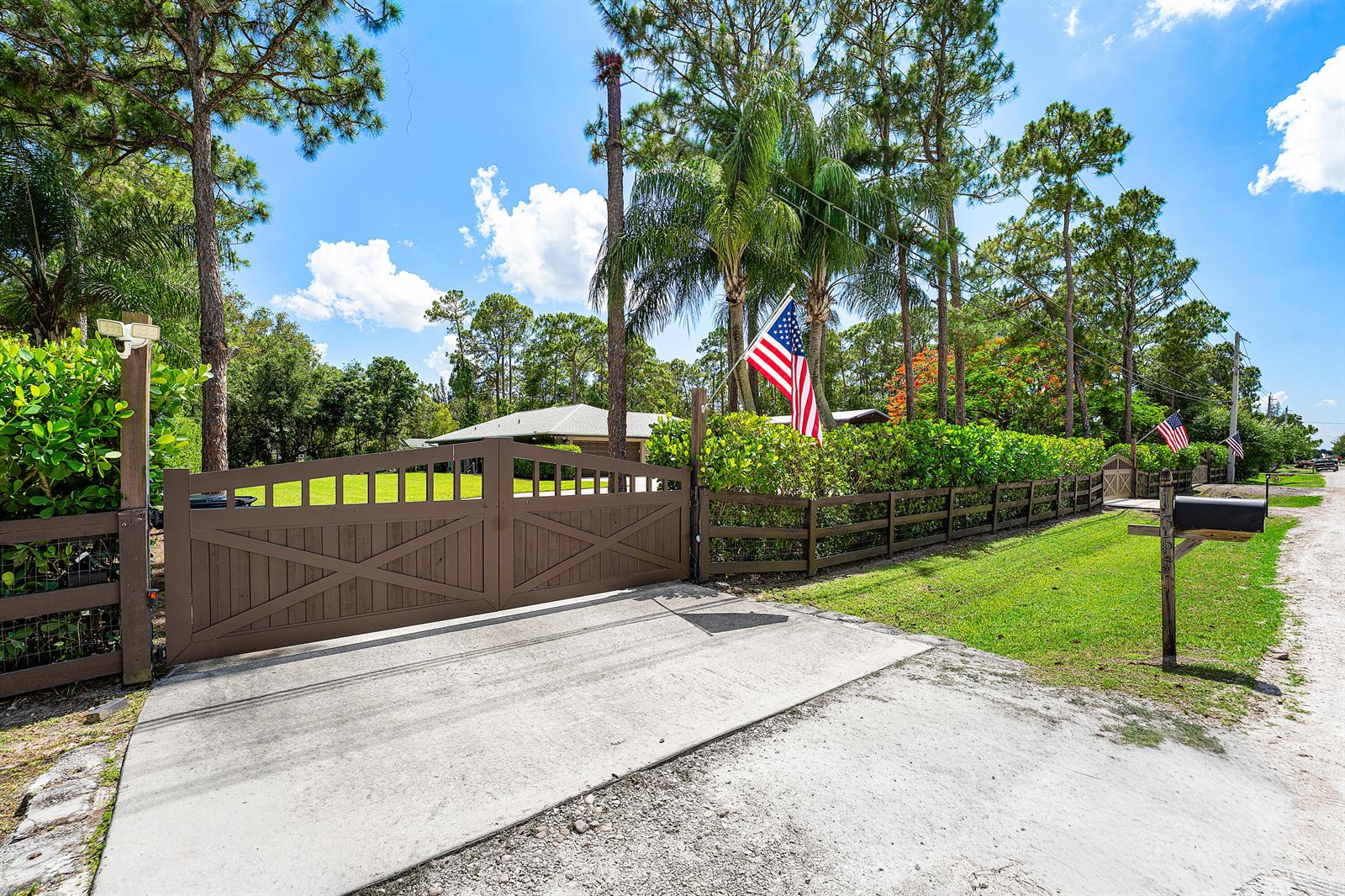 A brown wooden gate and fence enclose a property with a house and American flags — 13530 N 59th Ct Court N, FL 33411, FL