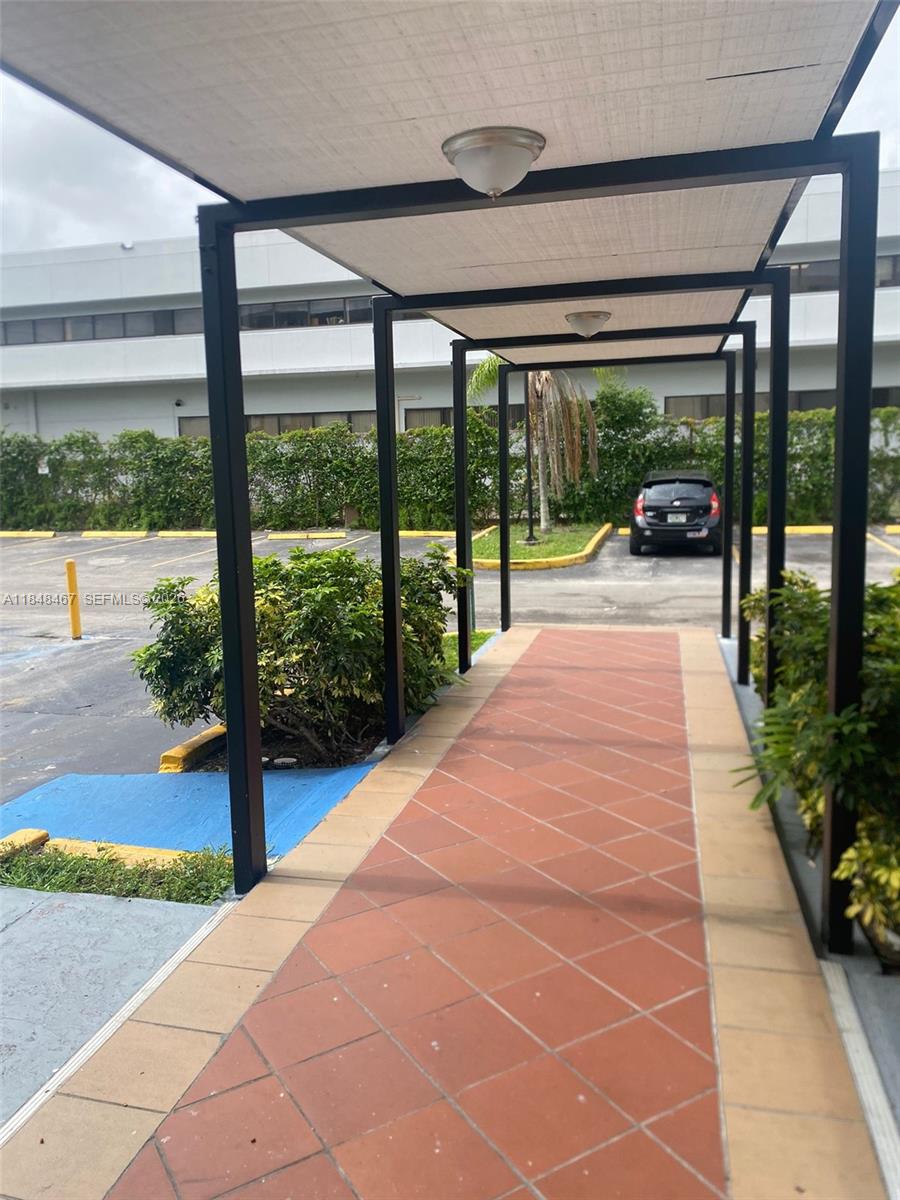 A covered walkway with a tiled path leads toward a parking lot with a car — 16450 NW 2nd Ave # 404, Miami FL 33169, MIAMI, FL