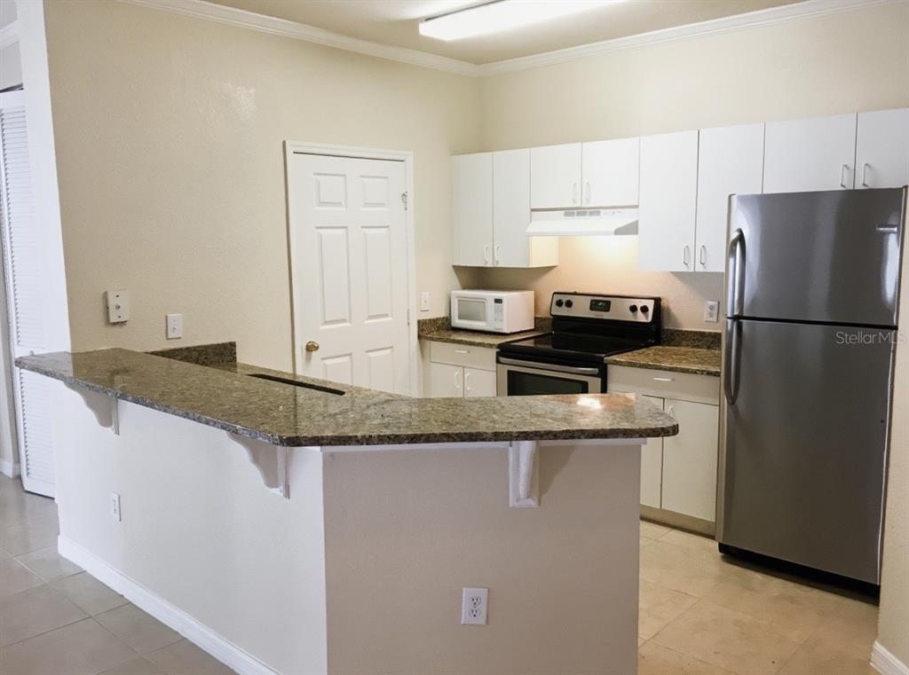 A kitchen features white cabinets, granite countertops, and stainless steel appliances with a breakfast bar — 3735 CONROY ROAD UNIT 2211, ORLANDO, FL