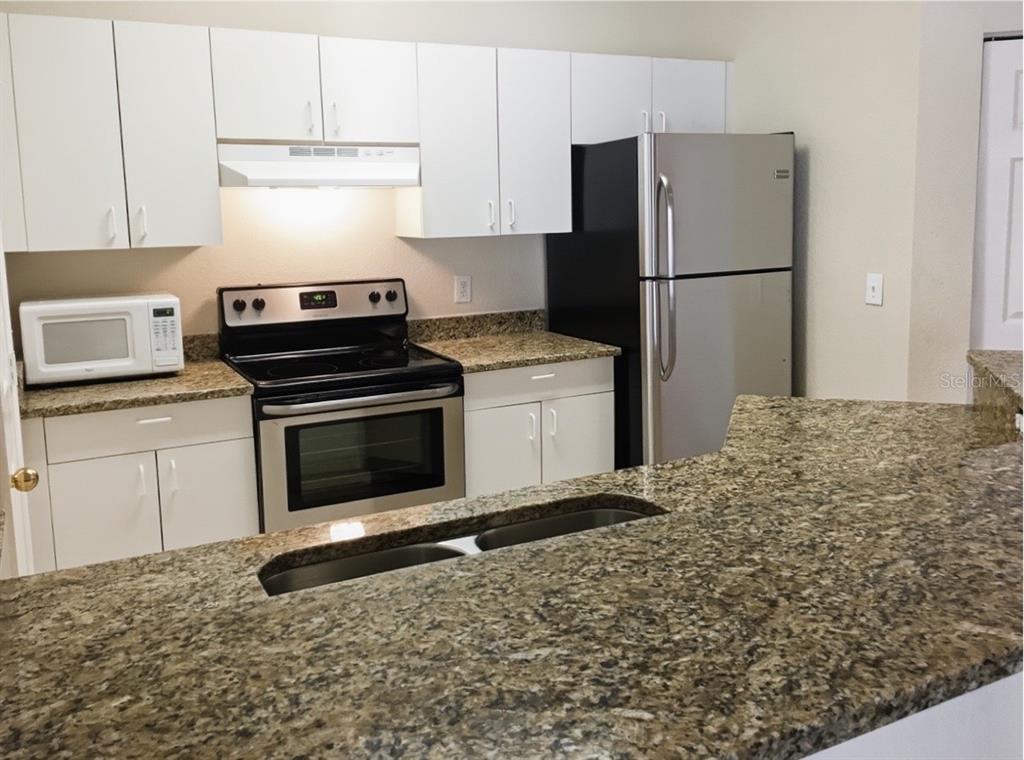 A kitchen features white cabinets, granite countertops, stainless steel appliances, and a breakfast bar — 3735 CONROY ROAD UNIT 2211, ORLANDO, FL