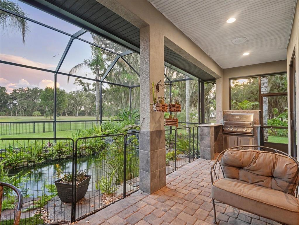 A covered patio features a built-in grill, a small pond, and a view of the yard — 339 CORBETT ROAD, LITHIA, FL