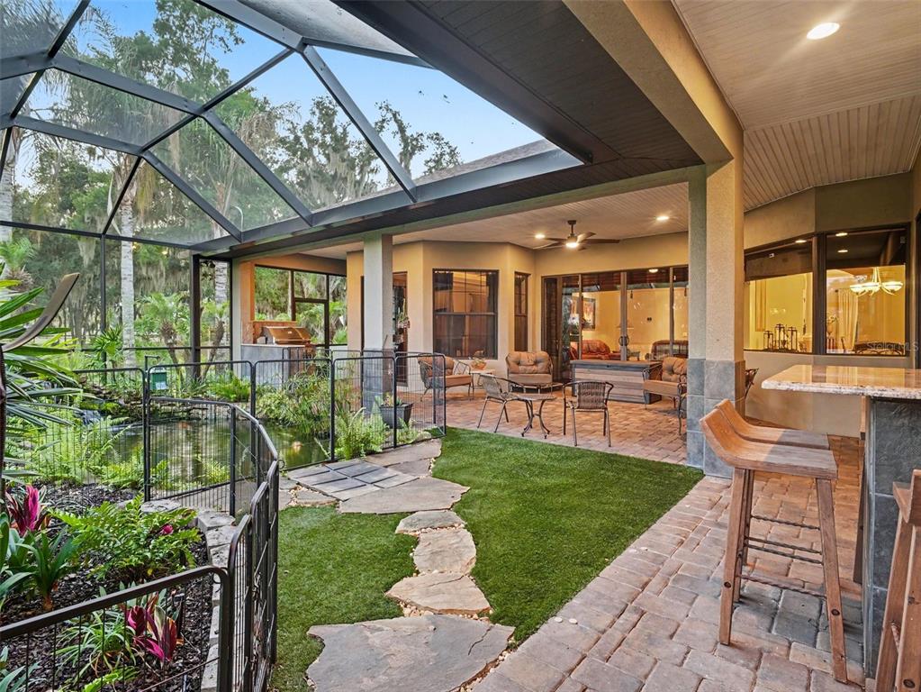 A screened-in patio features a small pond, artificial turf, stone pavers, and an outdoor bar — 339 CORBETT ROAD, LITHIA, FL