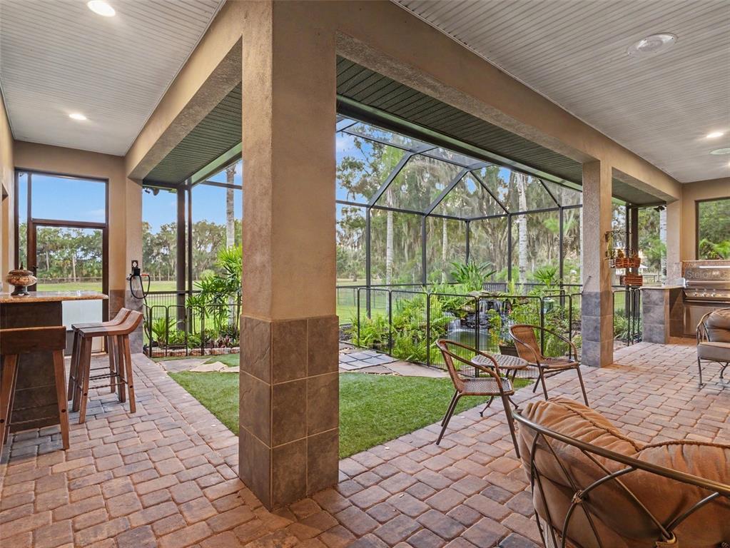 A covered patio with brick pavers, a bar, outdoor seating, and a screened-in pond area — 339 CORBETT ROAD, LITHIA, FL