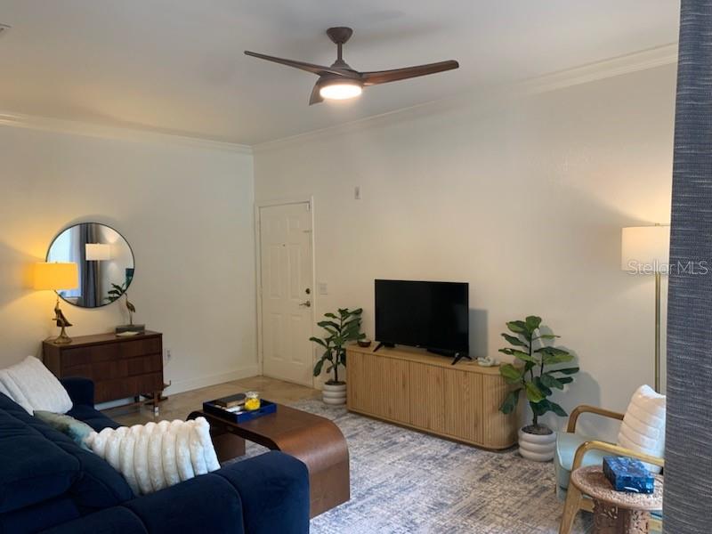 A living room features a blue sofa, a wooden media console, and a sliding glass door — 2200 TUSCANY TRACE UNIT 1714, PALM HARBOR, FL