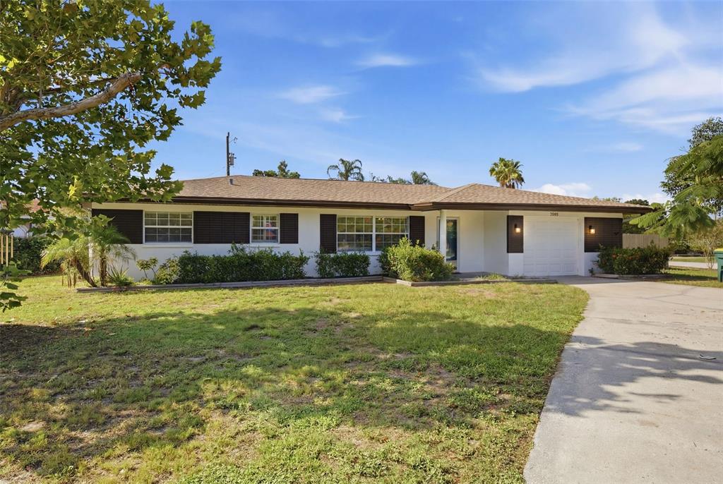 A single-story ranch-style house with a white exterior, dark shutters, and a concrete driveway — 2051 MAGNOLIA DRIVE, CLEARWATER, FL