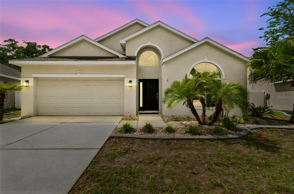 A single-story house with a two-car garage, arched windows, and a palm tree in front — 12155 INFINITY DRIVE, NEW PORT RICHEY, FL