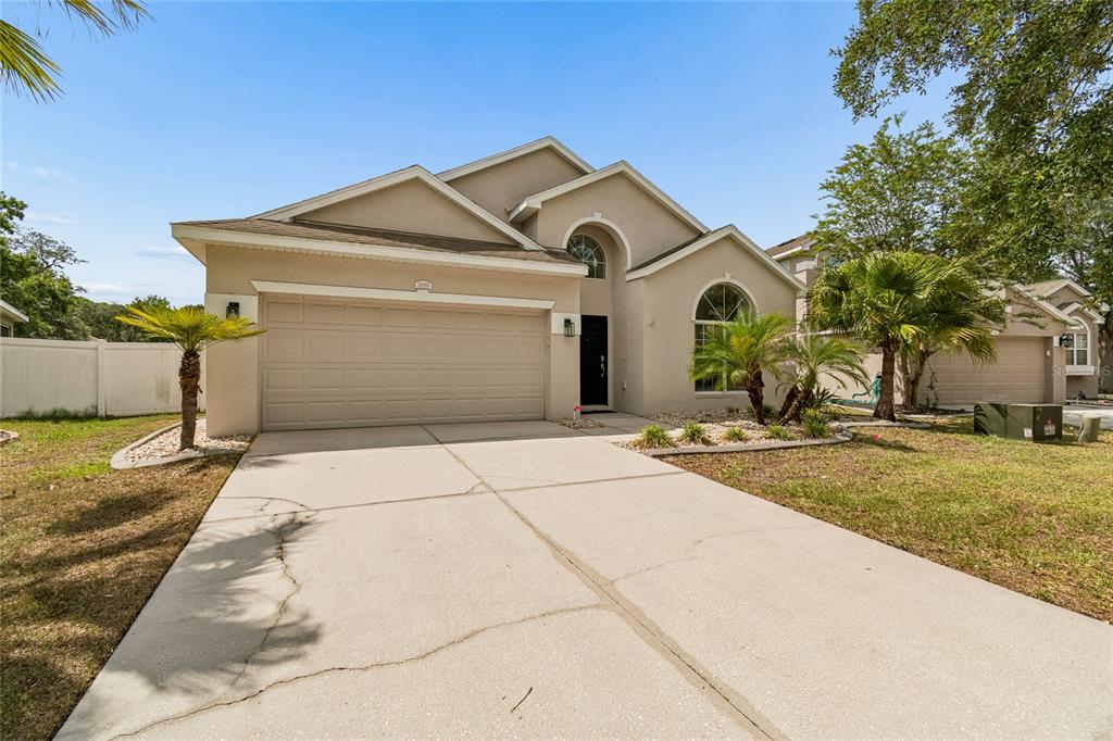 A beige single-story house with a two-car garage, arched windows, and a concrete driveway — 12155 INFINITY DRIVE, NEW PORT RICHEY, FL