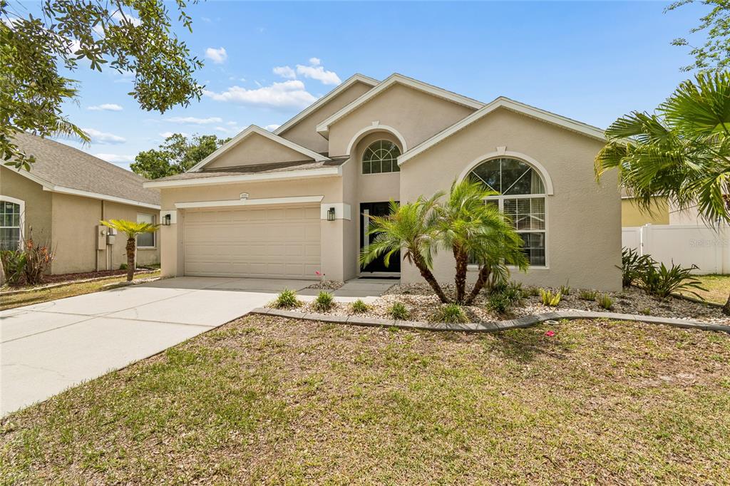 A beige single-story house features a two-car garage, arched windows, and a palm tree — 12155 INFINITY DRIVE, NEW PORT RICHEY, FL