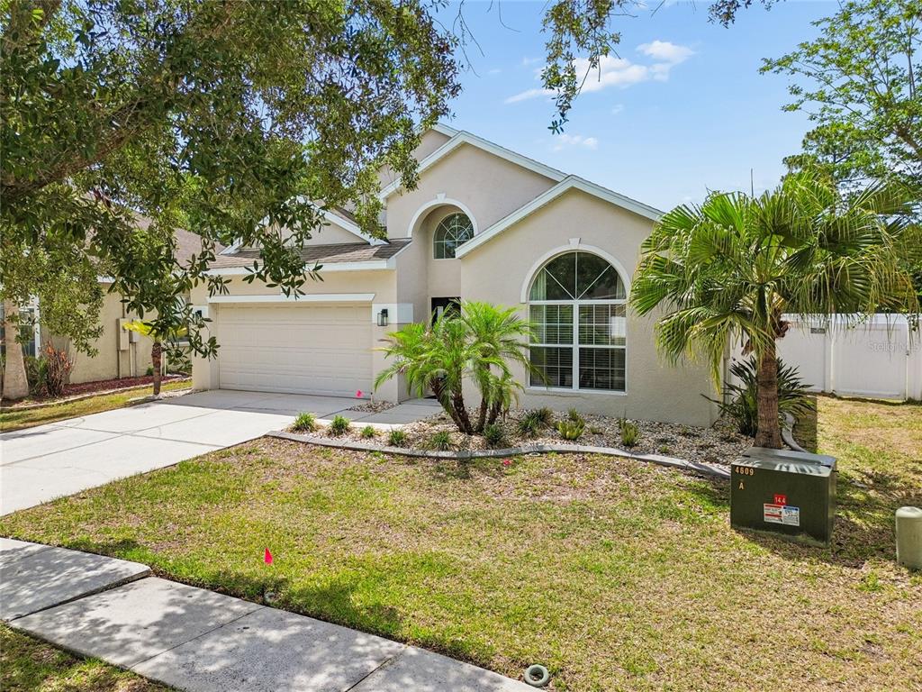 A single-story beige house with a two-car garage and a front yard with palm trees — 12155 INFINITY DRIVE, NEW PORT RICHEY, FL
