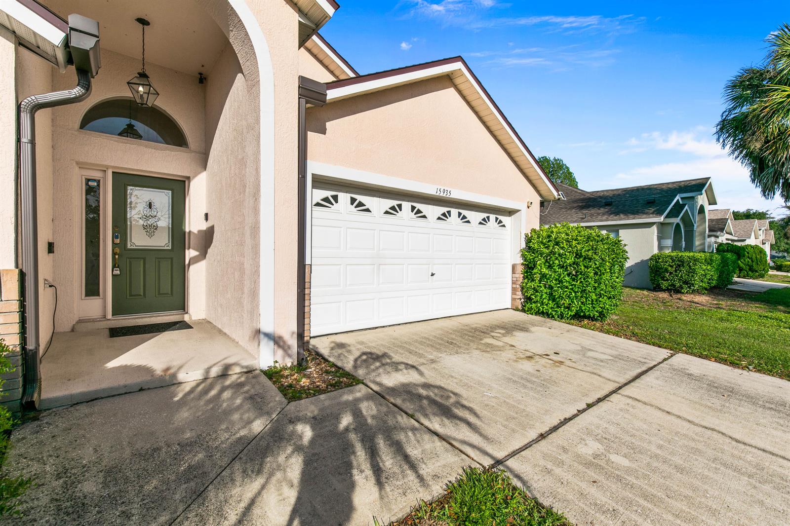 A beige house exterior features a green front door, a two-car garage, and a driveway — 15935 Heron Hill Street, Clermont FL 34714, CLERMONT, FL