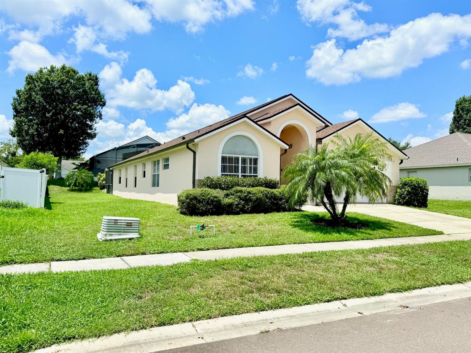 A single-story beige house with a palm tree, arched window, and a white fence — 15935 Heron Hill Street, Clermont FL 34714, CLERMONT, FL