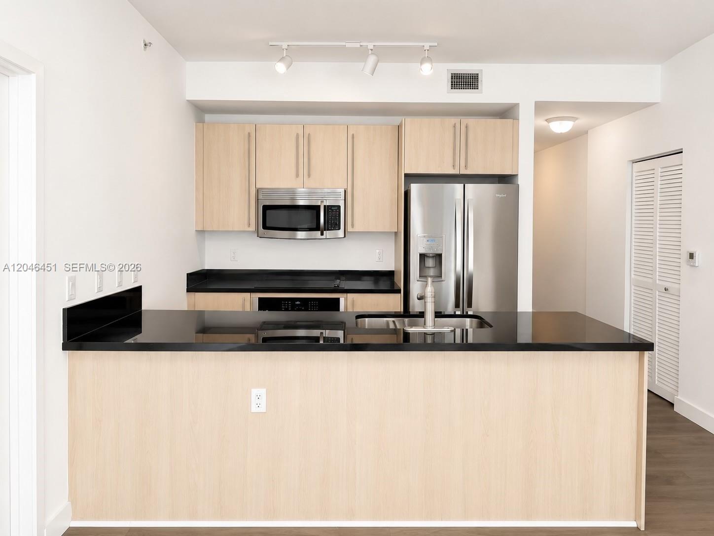 A kitchen features light wood cabinets, black countertops, and stainless steel appliances — 1111 SW 1st Ave, Miami FL 33130, MIAMI, FL