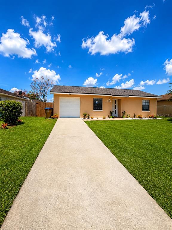 A single-story house with a tan exterior, a white garage door, and a concrete driveway — 348 CORNWALLIS COURT, KISSIMMEE, FL