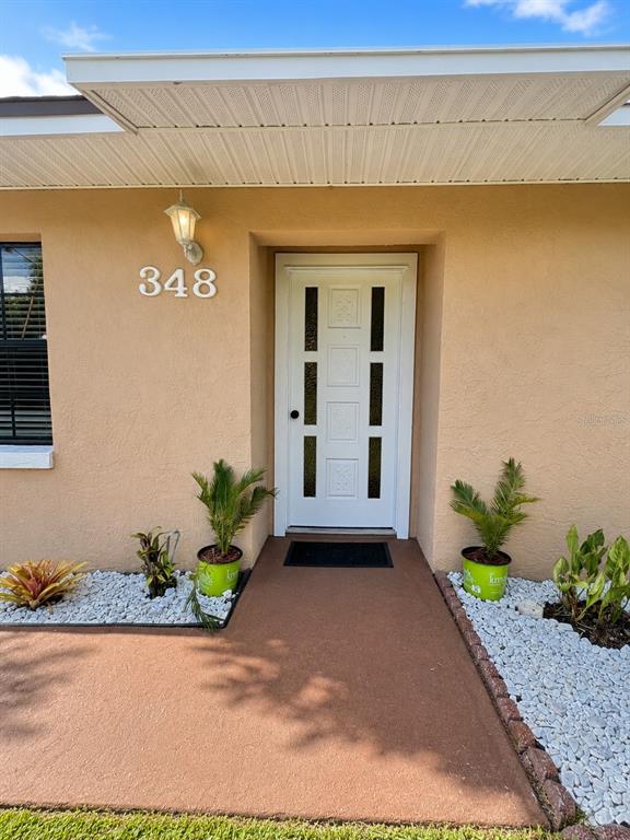 The exterior of a house features a white front door, address numbers, and potted plants — 348 CORNWALLIS COURT, KISSIMMEE, FL