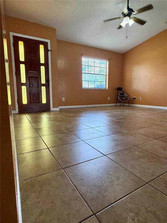 A living room with tan walls, tile flooring, a ceiling fan, and a front door — 348 CORNWALLIS COURT, KISSIMMEE, FL
