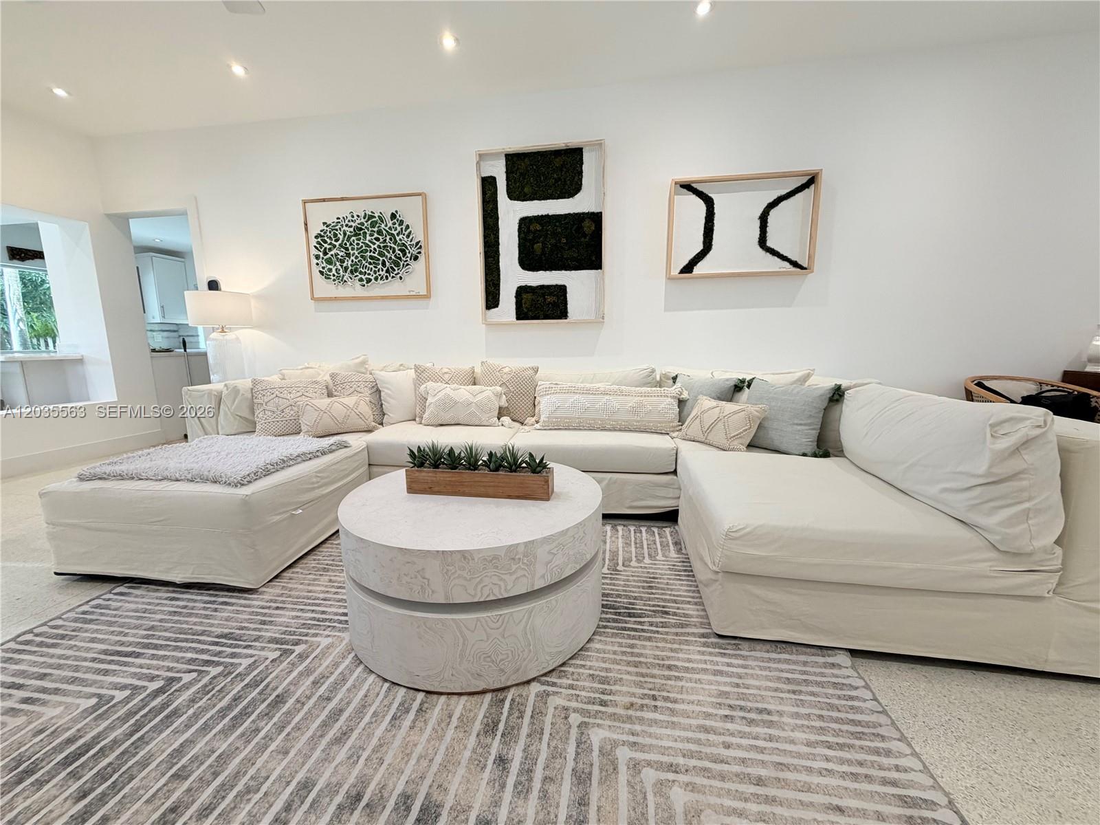 A living room features a large white sectional sofa, a round coffee table, and wall art — 1460 Cleveland Rd, Miami Beach FL 33141, MIAMI BEACH, FL