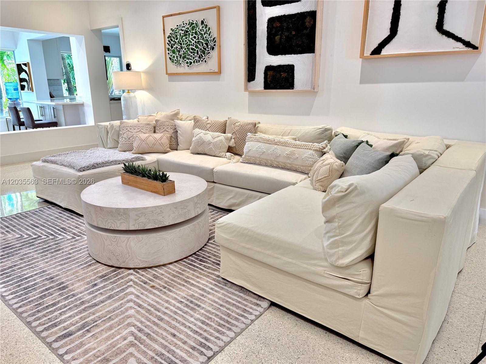 A living room features a large cream sectional sofa, a round coffee table, and textured artwork — 1460 Cleveland Rd, Miami Beach FL 33141, MIAMI BEACH, FL