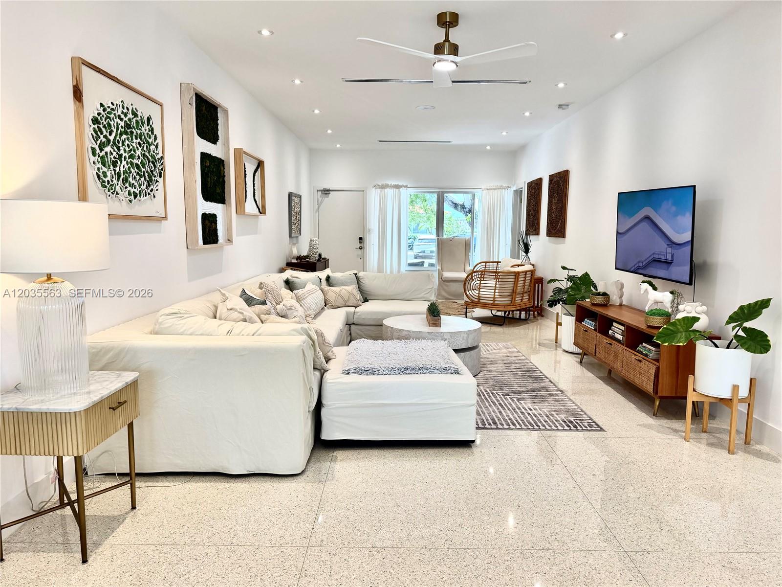 A bright living room features a large white sectional sofa, a television, and tiled floors — 1460 Cleveland Rd, Miami Beach FL 33141, MIAMI BEACH, FL