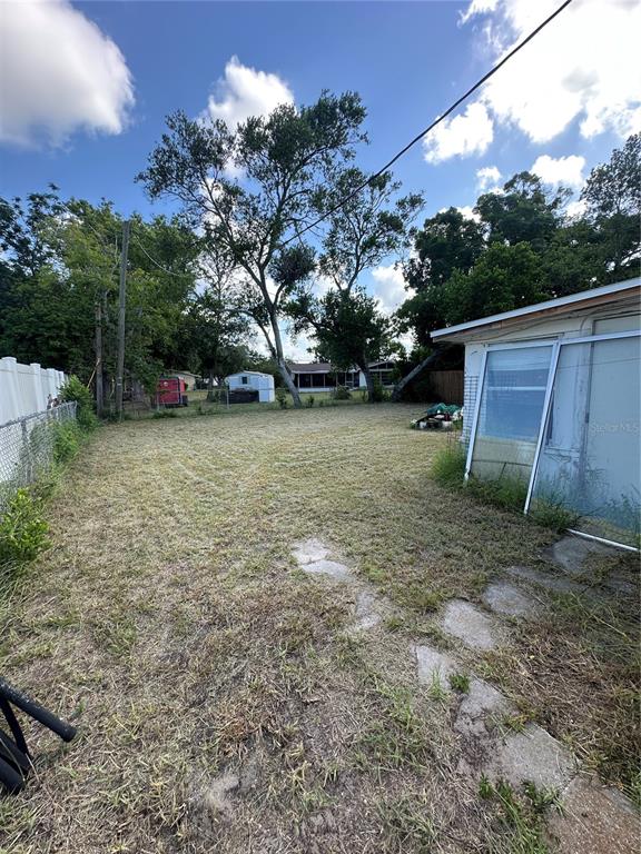 A grassy backyard features a white fence, mature trees, and a house with sliding doors — 4923 STATE ROAD 54, NEW PORT RICHEY, FL