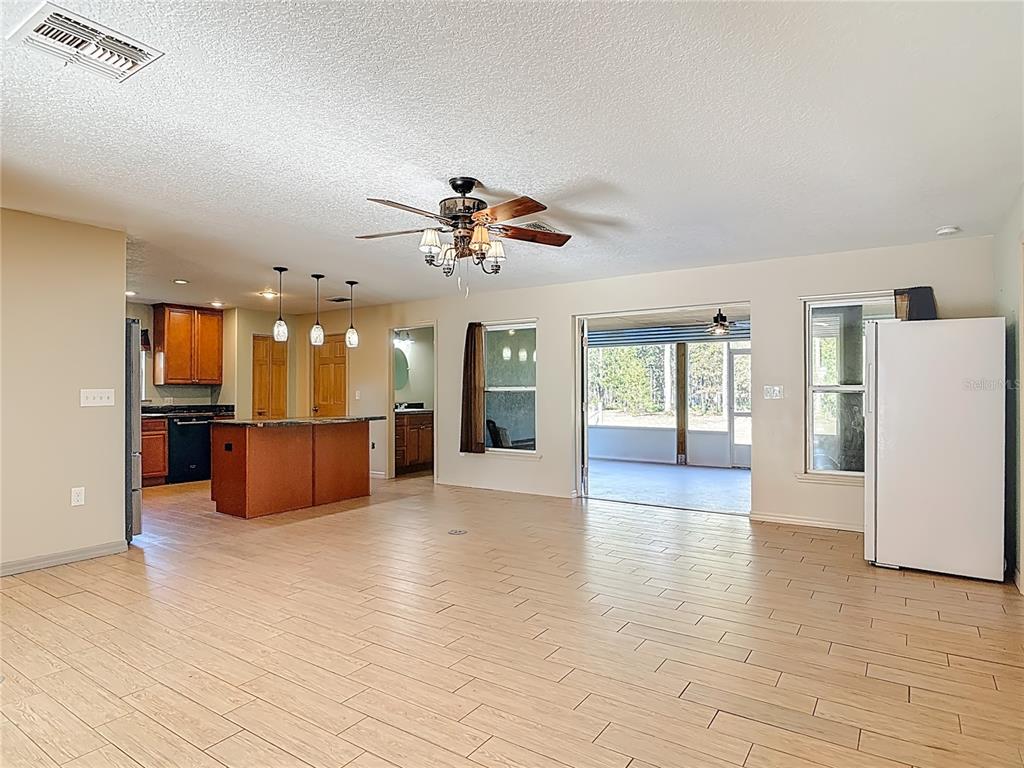 An open-concept living area features wood-look tile flooring, a kitchen island, and a sliding glass door — 6100 WINNING WOOD TRAIL, DE LEON SPRINGS, FL