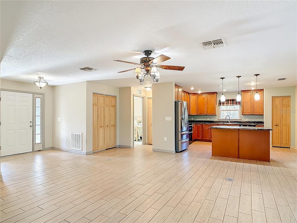 An open-concept kitchen and living area featuring wood-look tile flooring and light-colored walls — 6100 WINNING WOOD TRAIL, DE LEON SPRINGS, FL