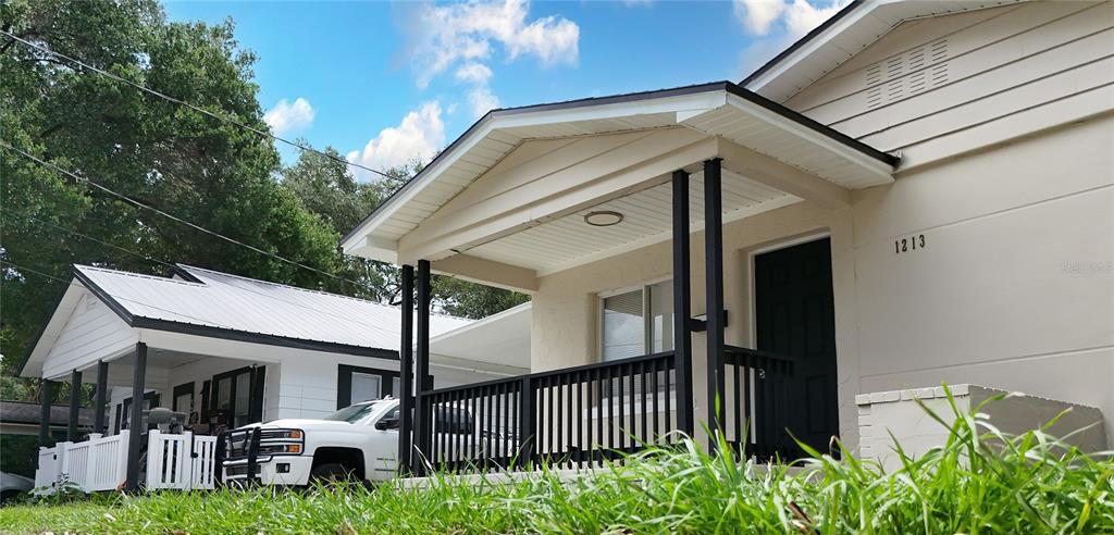 A low-angle exterior view of a beige house with a covered porch and black railings — 1213 E 24TH AVENUE, TAMPA, FL