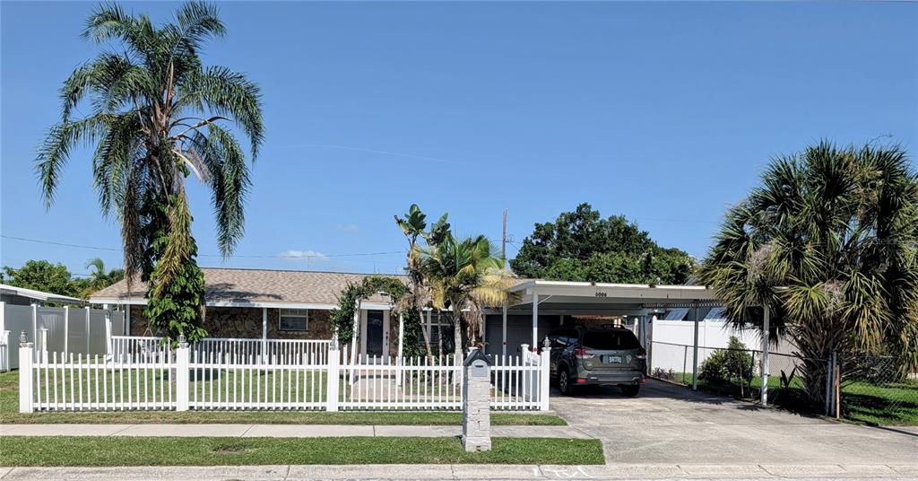 A single-story house with a white picket fence, a carport, and two large palm trees — 6006 N HUBERT AVE, TAMPA, FL