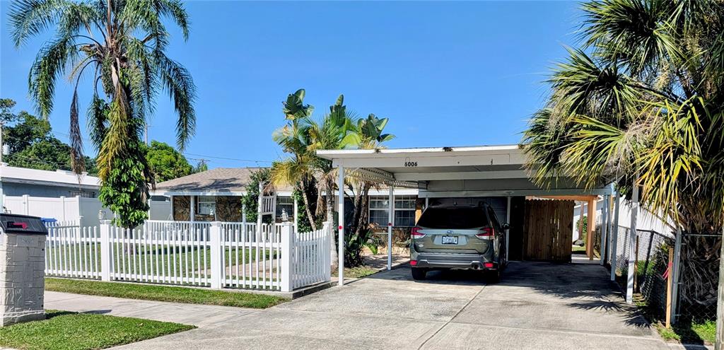 A single-story house features a white picket fence, a carport, and palm trees — 6006 N HUBERT AVE, TAMPA, FL