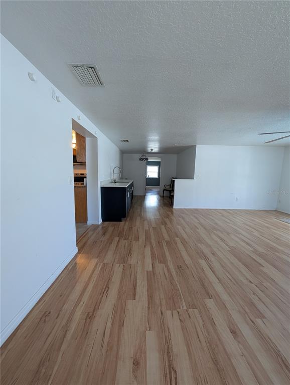 A spacious room with light wood-look flooring leads to a kitchen with dark cabinets — 6006 N HUBERT AVE, TAMPA, FL