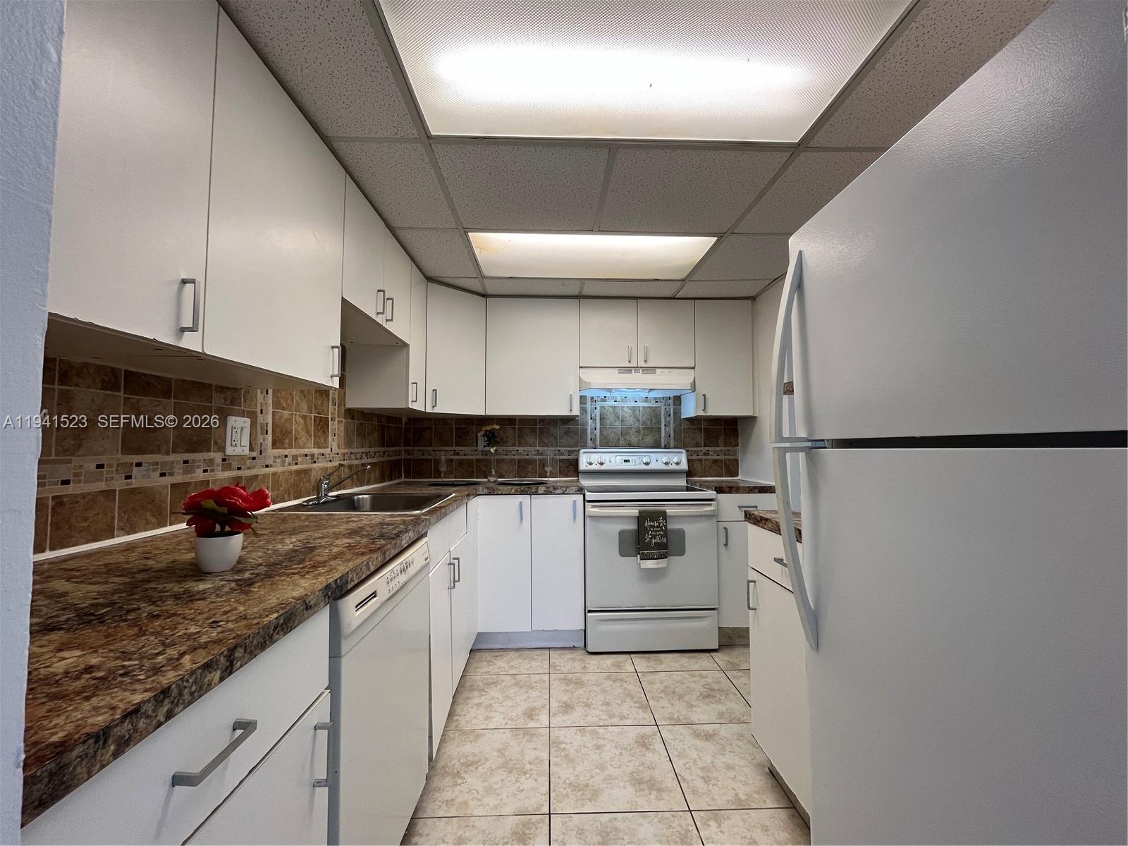 A kitchen features white cabinets, a brown patterned countertop, white appliances, and tiled flooring — 4354 NW 9th Ave # 1C, Deerfield Beach FL 33064, DEERFIELD BEACH, FL