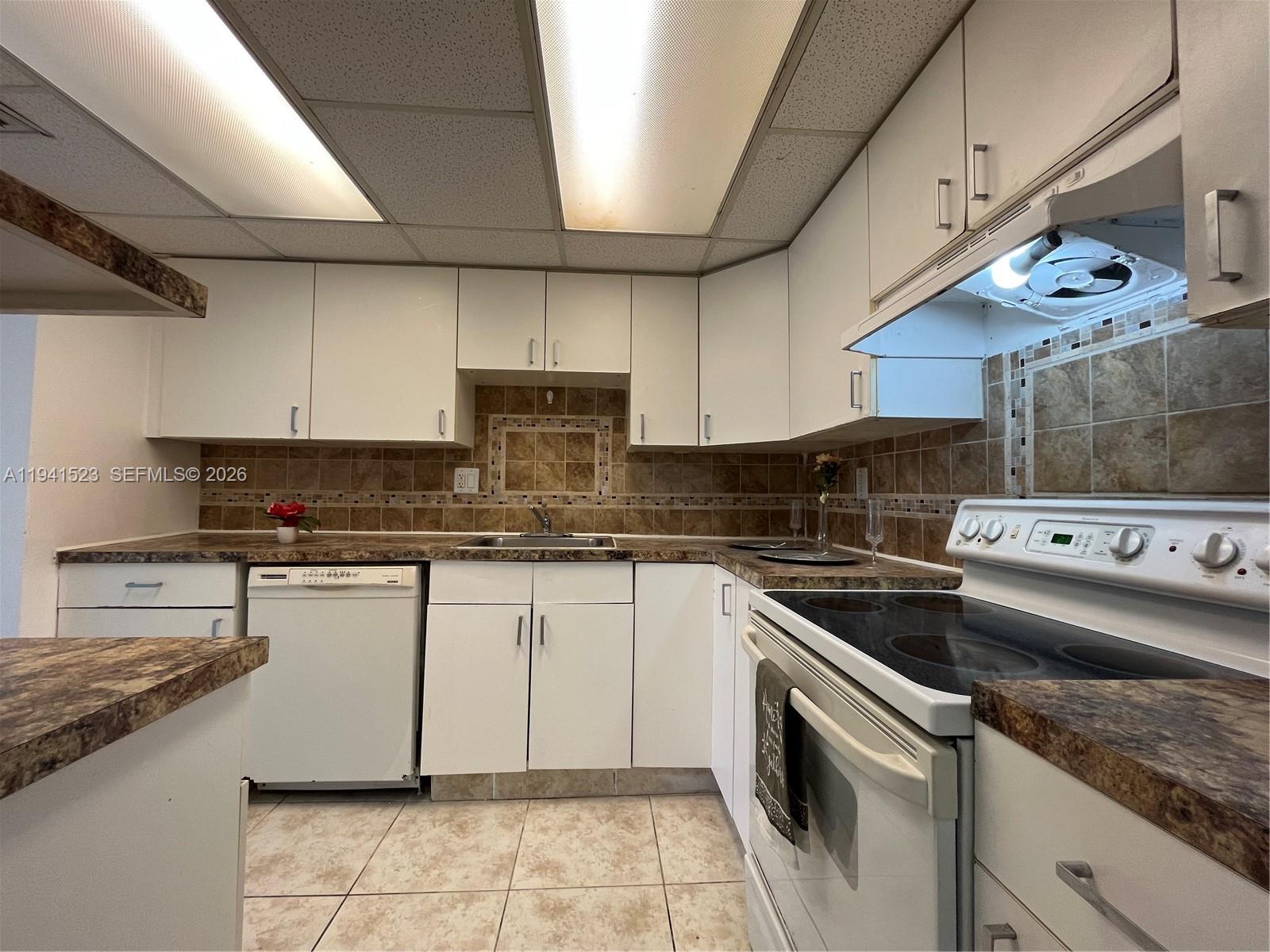 A kitchen features white cabinets, brown laminate countertops, tiled backsplash, and white appliances — 4354 NW 9th Ave # 1C, Deerfield Beach FL 33064, DEERFIELD BEACH, FL