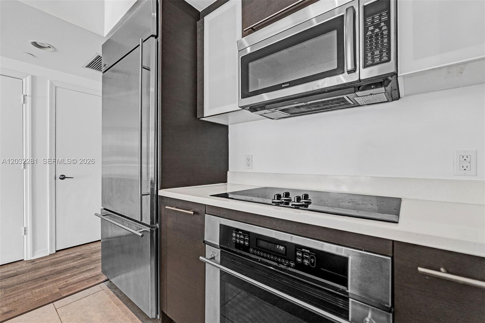 A modern kitchen features dark wood cabinets, stainless steel appliances, and a white countertop — 55 SE 6th St # 1208, Miami FL 33131, MIAMI, FL