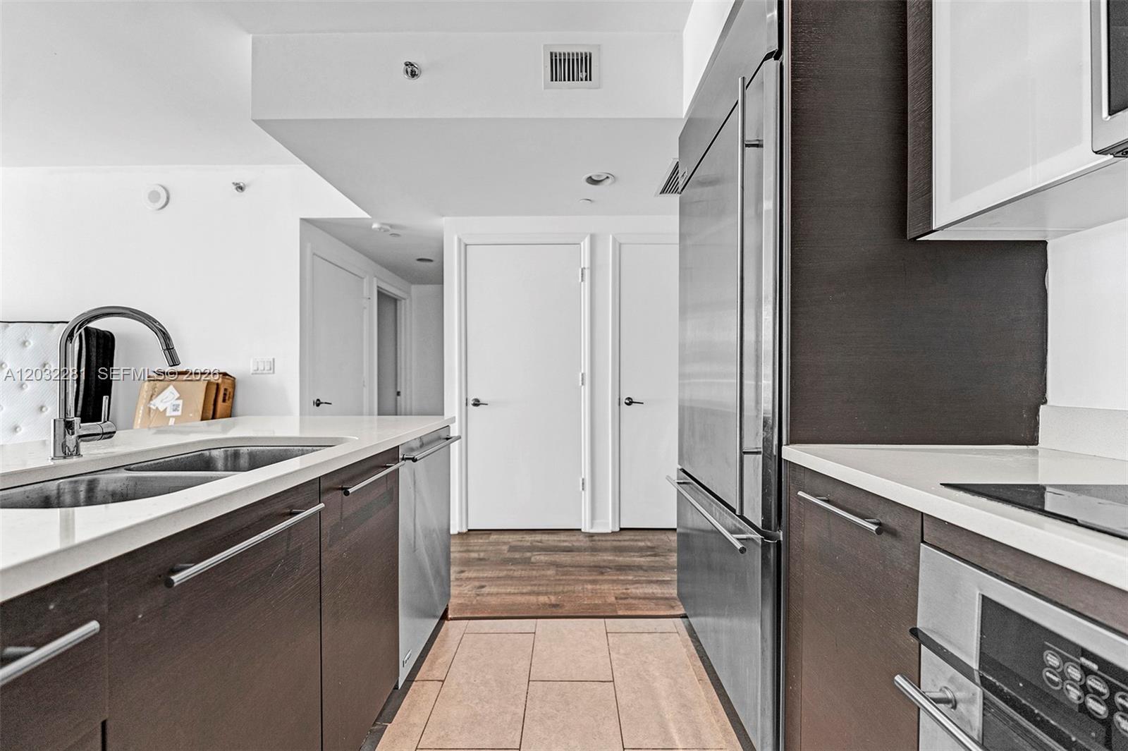 A modern kitchen features dark wood cabinets, stainless steel appliances, and light-colored countertops — 55 SE 6th St # 1208, Miami FL 33131, MIAMI, FL