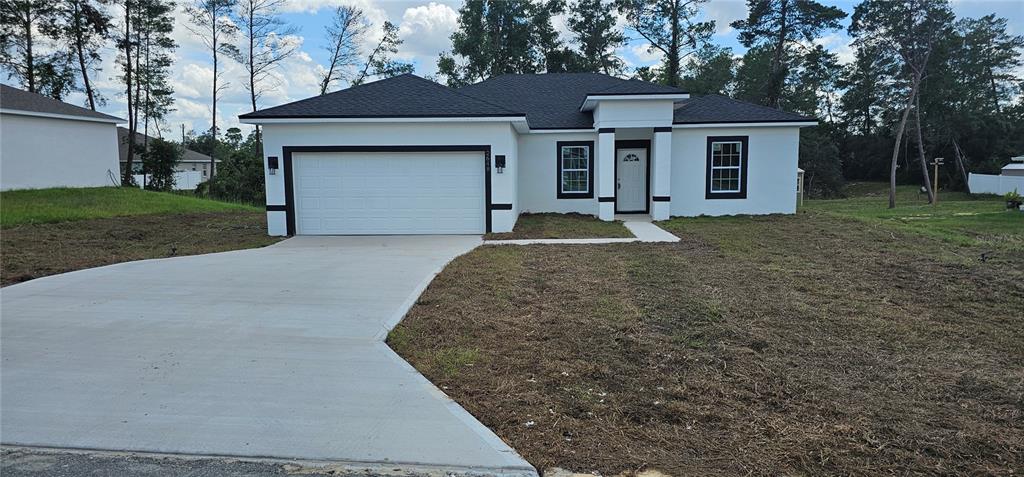A single-story house features a white stucco exterior, black trim, and a two-car garage — 2648 SW 146 TH PLACE ROAD, OCALA, FL