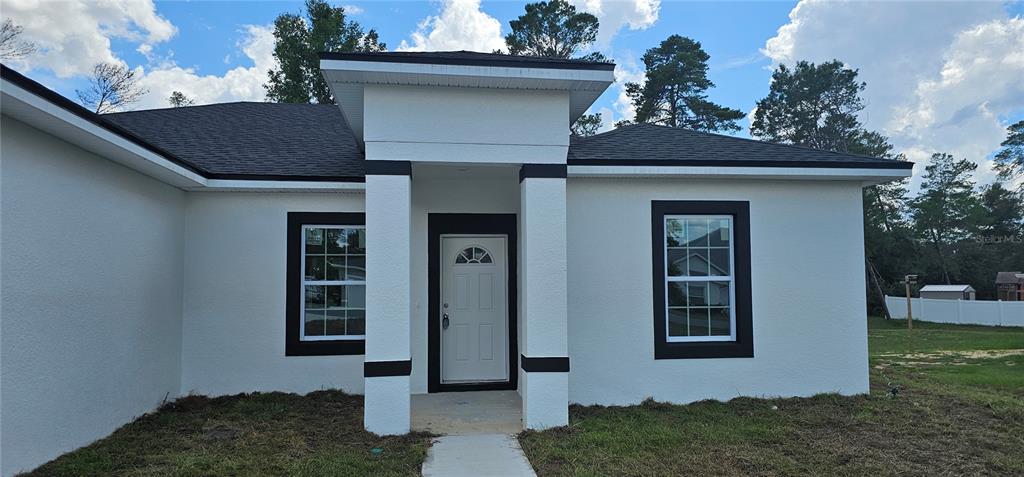 A white house with a black-trimmed entryway and windows stands under a blue sky — 2648 SW 146 TH PLACE ROAD, OCALA, FL