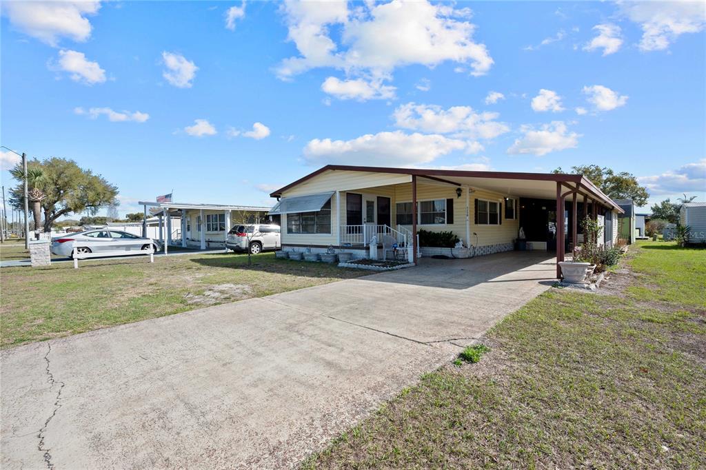 A yellow manufactured home with a concrete driveway and an attached carport under a sky — 5250 DEAN DAIRY ROAD, ZEPHYRHILLS, FL