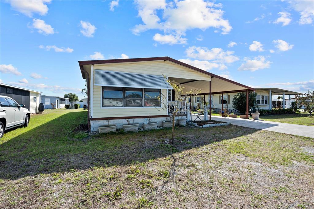 A single-story manufactured home features light yellow siding, a carport, and a front lawn — 5250 DEAN DAIRY ROAD, ZEPHYRHILLS, FL