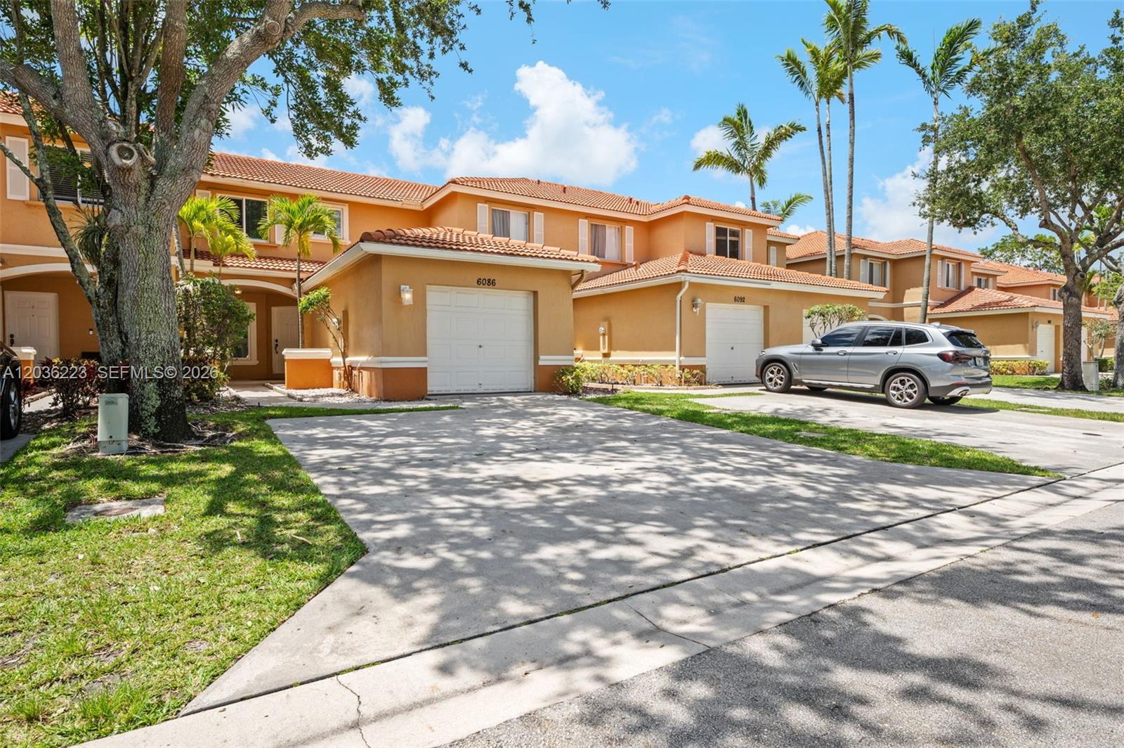 A two-story townhouse with a tan stucco exterior, tile roof, and a concrete driveway — 6086 Southard St, West Palm Beach FL 33411, WEST PALM BEACH, FL